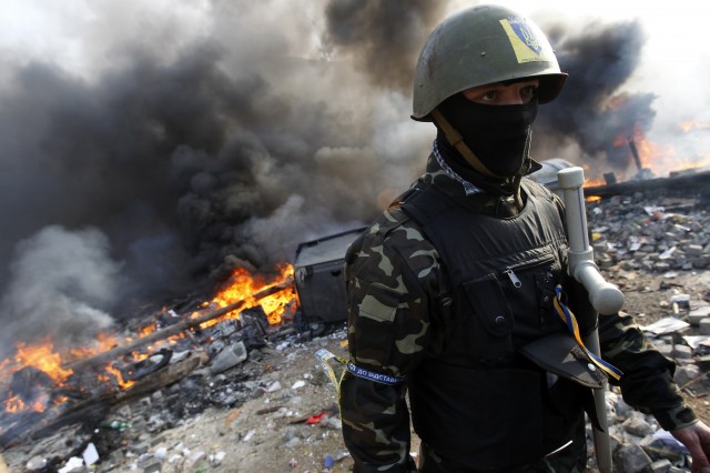 An anti-government protester looks on as smoke from a fire rises above Independence Square in central Kiev